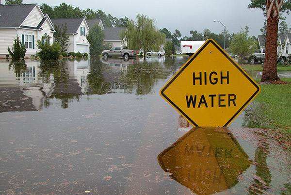 Flooded street in suburban neighborhood; water up to High Water sign